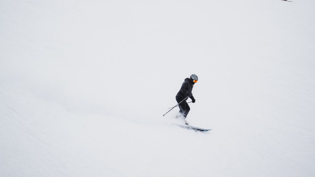 man in black jacket and black pants riding ski blades on snow covered ground during daytime